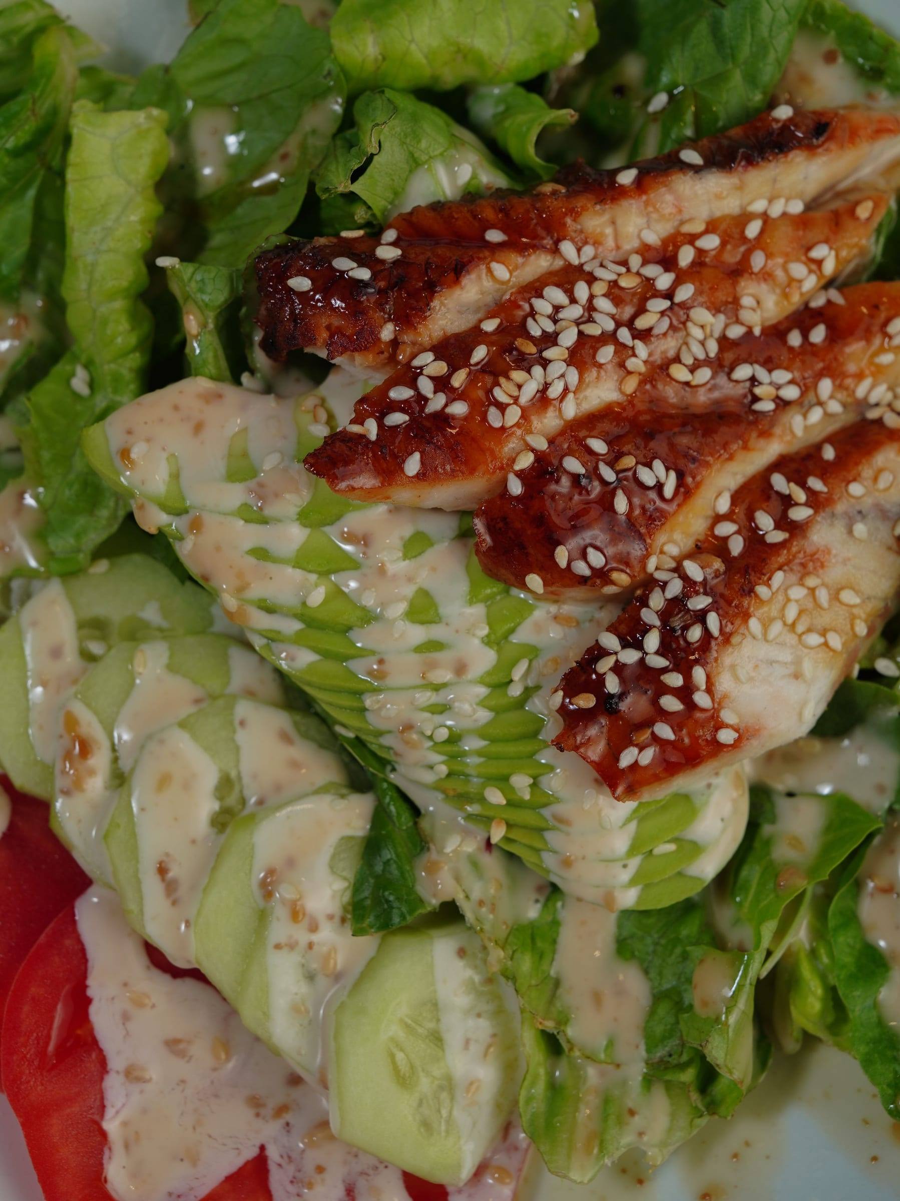 Gegrillte Hähnchenbrust in Streifen mit Sesam auf Salat mit Avocado und hellem Dressing