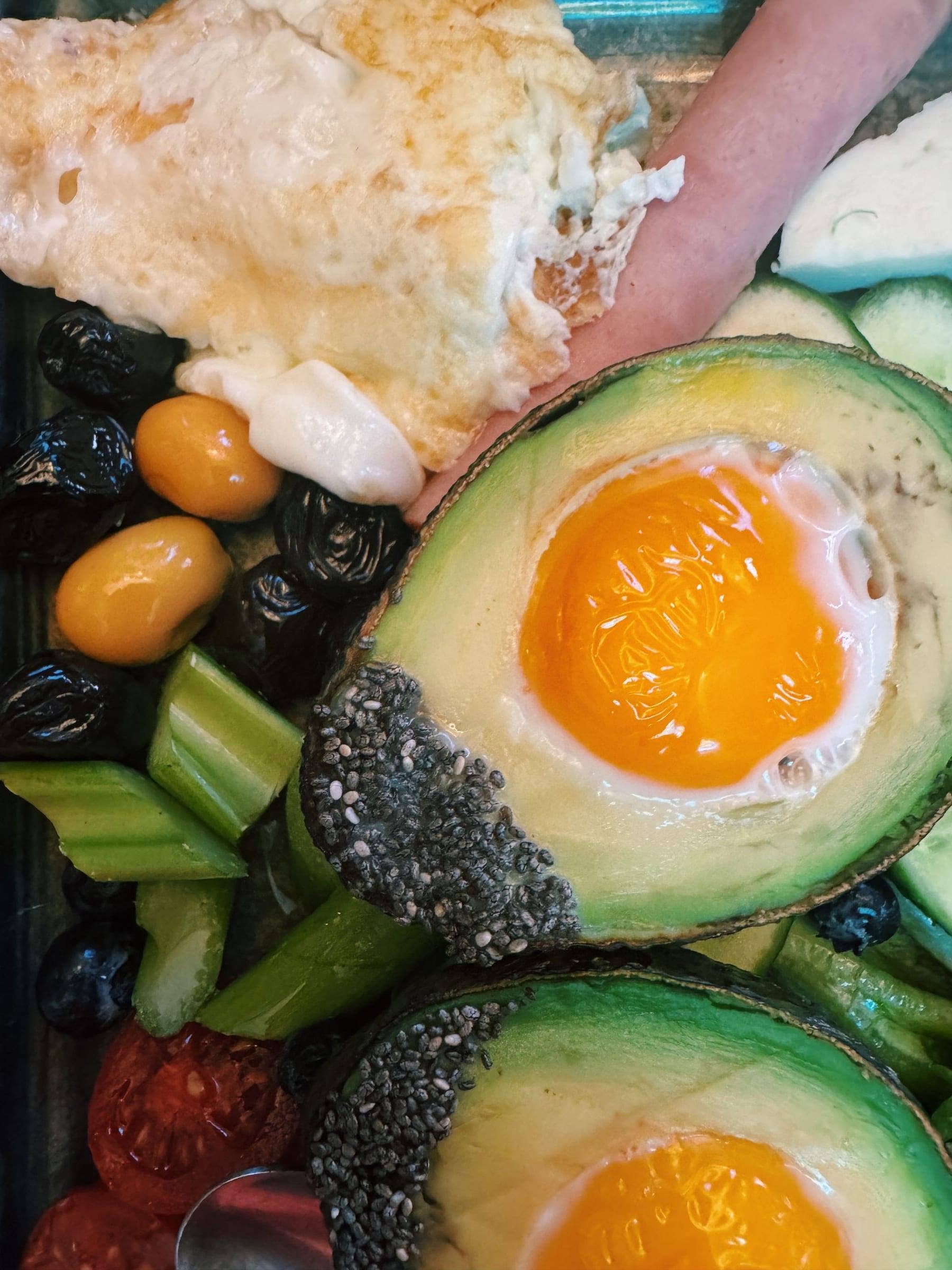 Spiegelei in einer Avocadohälfte, umgeben von Oliven, Sellerie und Chiasamen