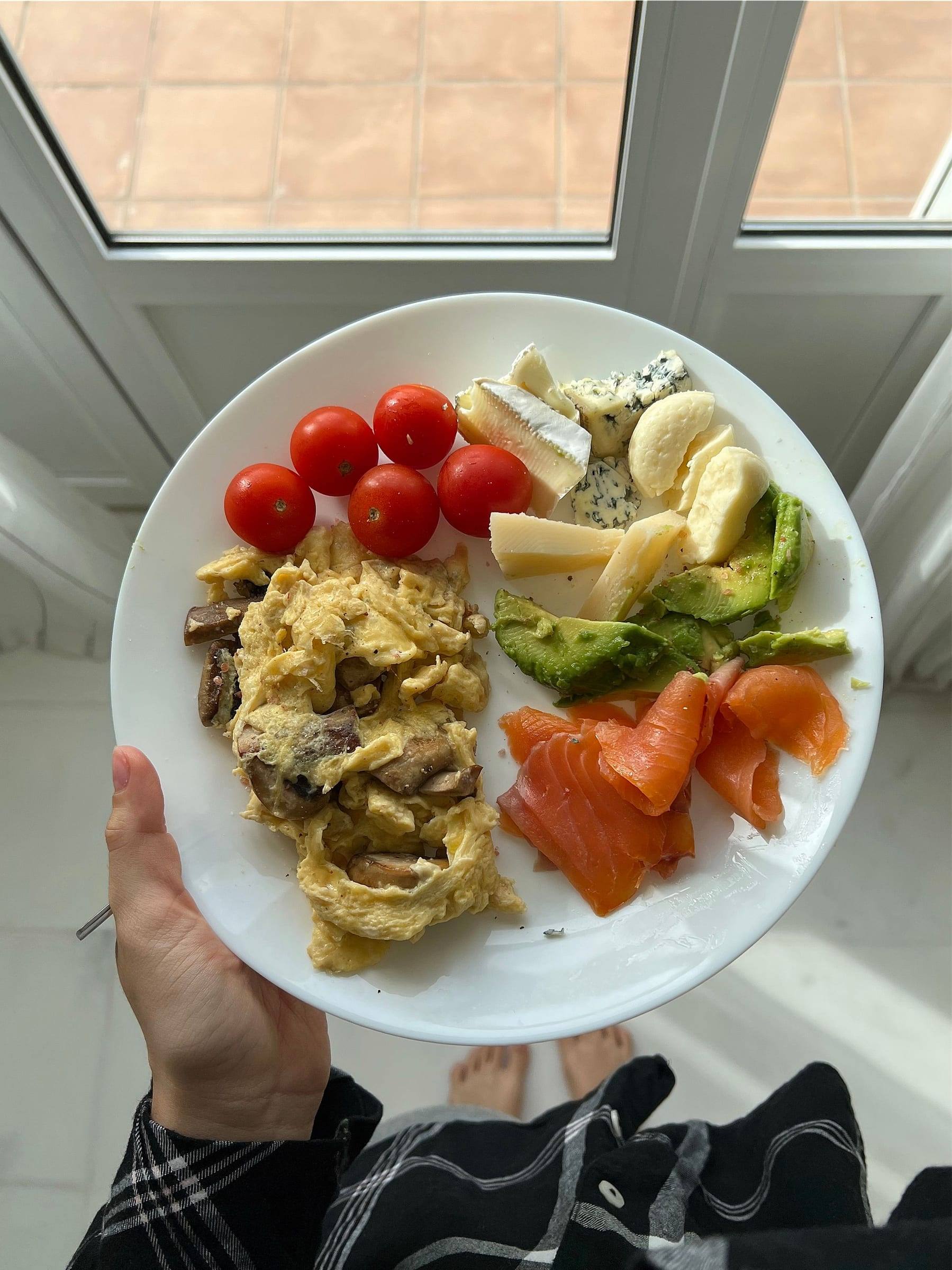 Teller mit Rührei, Avocado, Räucherlachs, Kirschtomaten und verschiedenen Käsesorten